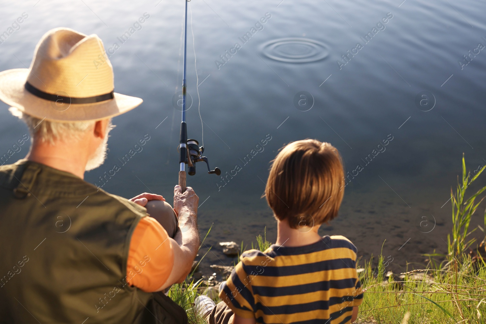 Grandfather and his nephew fishing together near river outdoors, back view Photo of Grandfather and his nephew fishing together near river outdoors, back view