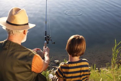 Photo of Grandfather and his nephew fishing together near river outdoors, back view