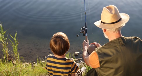 Photo of Grandfather and his nephew fishing together near river outdoors, back view