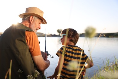 Photo of Happy grandfather and his nephew fishing together near river outdoors