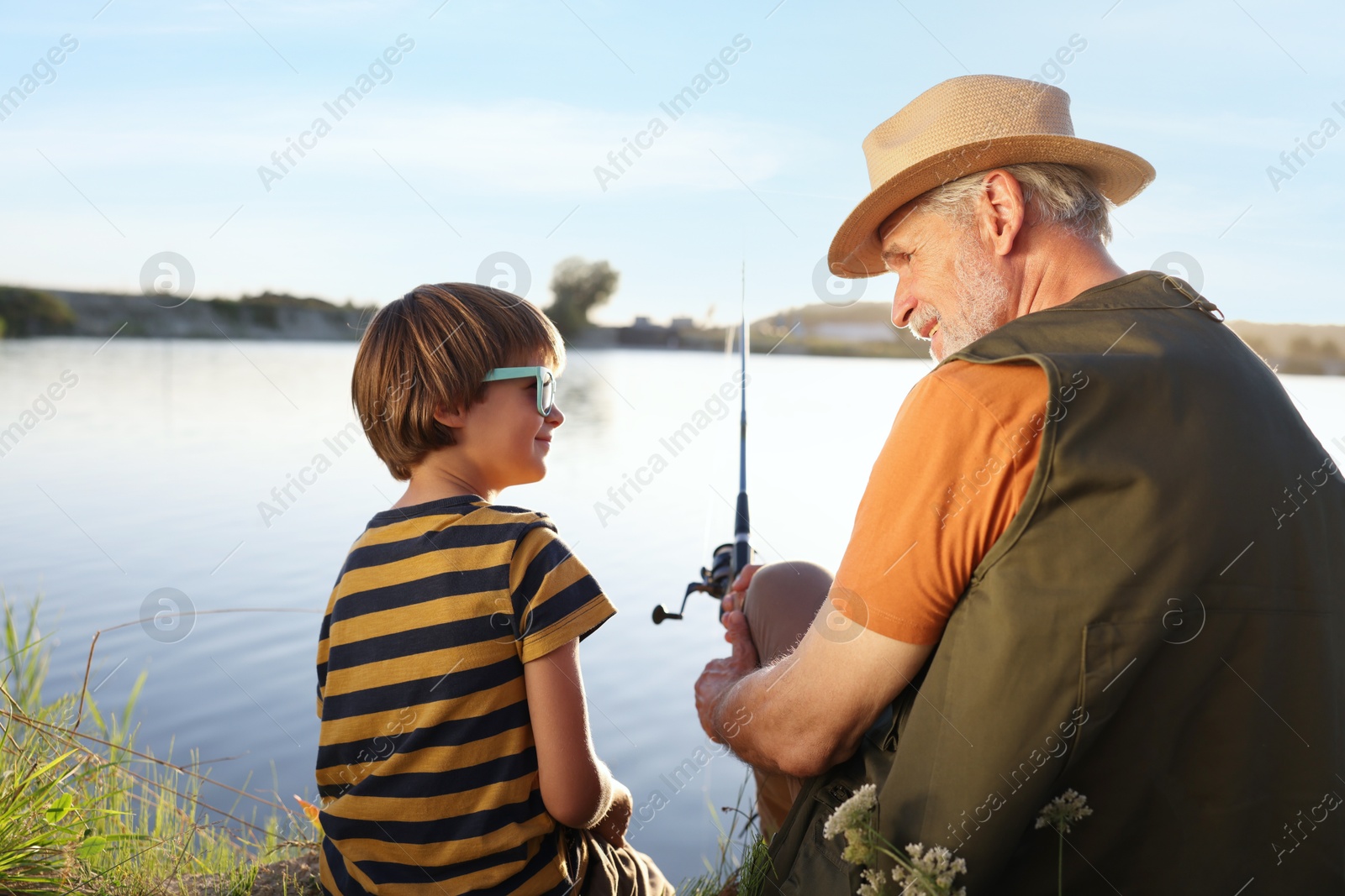 Photo of Happy grandfather and his nephew fishing together near river outdoors