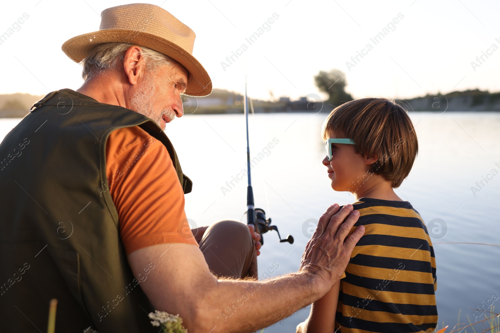 Photo of Happy grandfather and his nephew fishing together near river outdoors