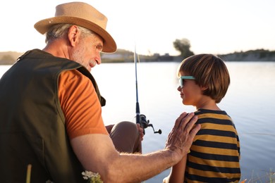 Photo of Happy grandfather and his nephew fishing together near river outdoors