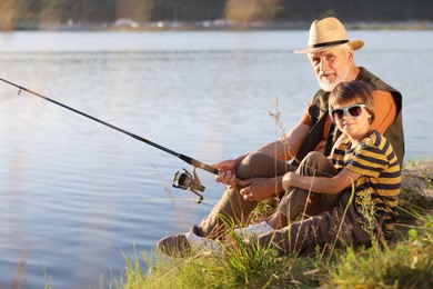 Photo of Grandfather and his nephew fishing together near river outdoors