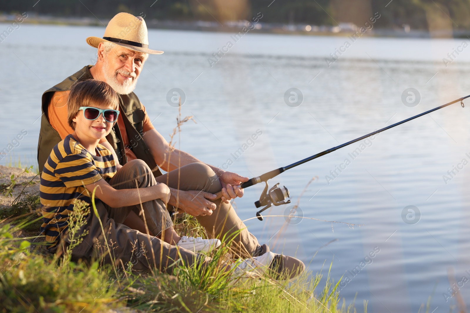 Photo of Happy grandfather and his nephew fishing together near river outdoors