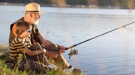 Photo of Grandfather and his nephew fishing together near river outdoors