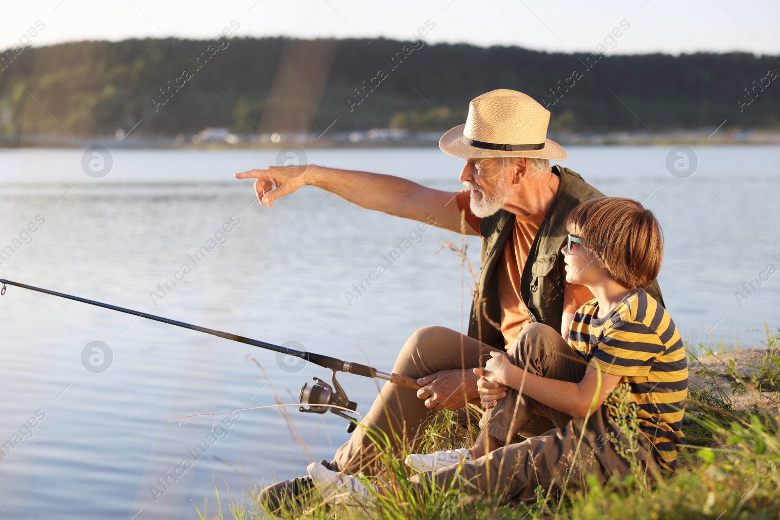 Grandfather and his nephew fishing together near river outdoors Photo of Grandfather and his nephew fishing together near river outdoors
