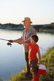 Photo of Grandfather and his nephew fishing together near river outdoors