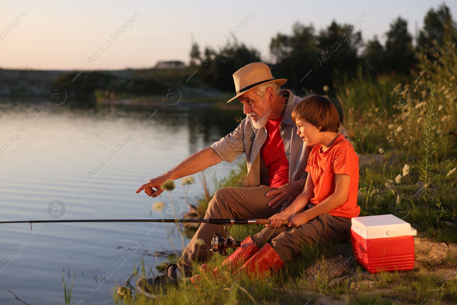 Grandfather and his nephew fishing together near river outdoors Photo of Grandfather and his nephew fishing together near river outdoors