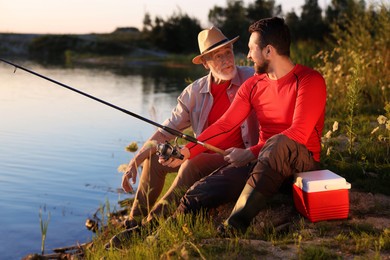Photo of Elderly father and his happy son fishing together near river outdoors