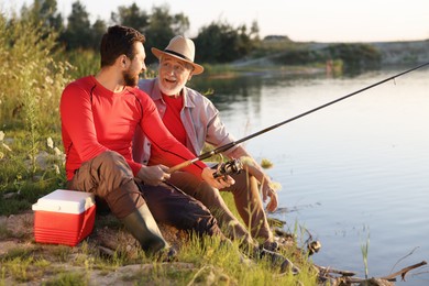 Photo of Elderly father and his happy son fishing together near river outdoors
