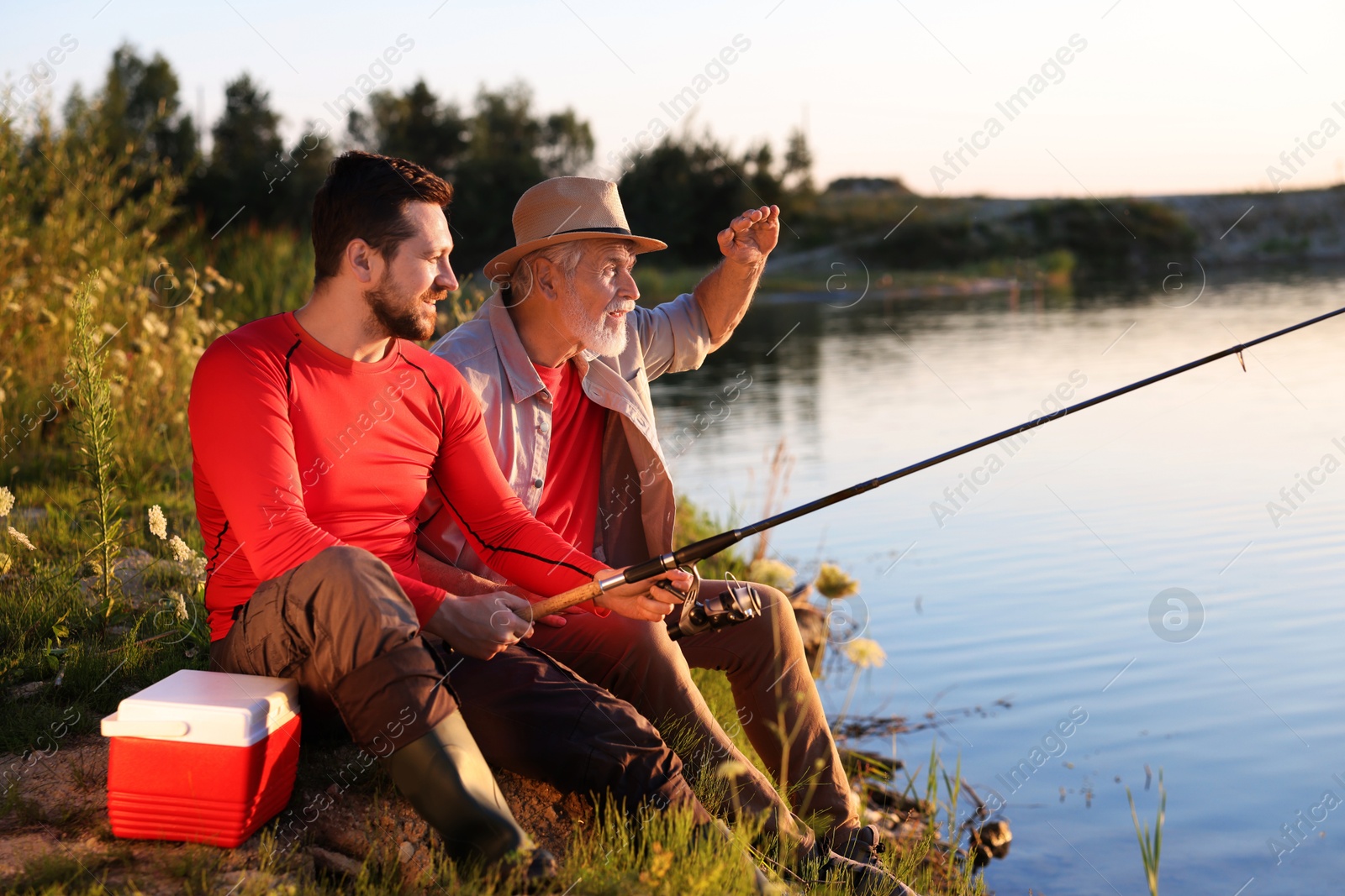 Elderly father and his happy son fishing together near river outdoors Photo of Elderly father and his happy son fishing together near river outdoors
