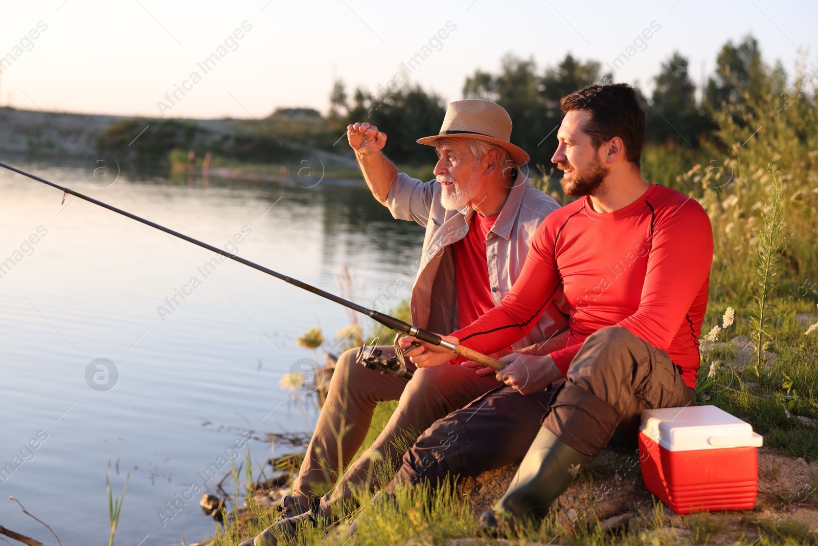 Photo of Elderly father and his happy son fishing together near river outdoors
