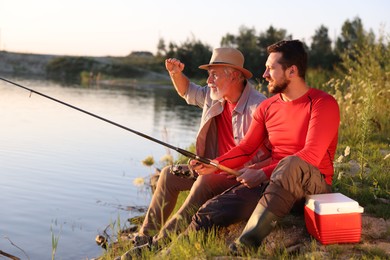 Photo of Elderly father and his happy son fishing together near river outdoors