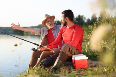 Photo of Emotional elderly father and his son fishing together near river outdoors