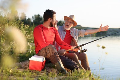 Photo of Emotional elderly father and his son fishing together near river outdoors