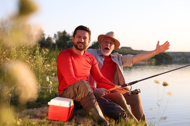 Photo of Emotional elderly father and his happy son fishing together near river outdoors
