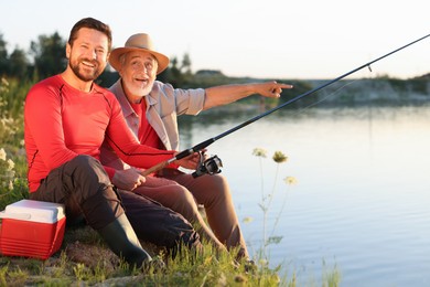 Photo of Happy elderly father and his son fishing together near river outdoors