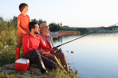 Photo of Grandfather, father and his little son fishing together near river outdoors