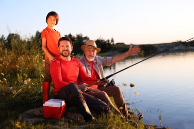 Photo of Grandfather, father and his little son fishing together near river outdoors