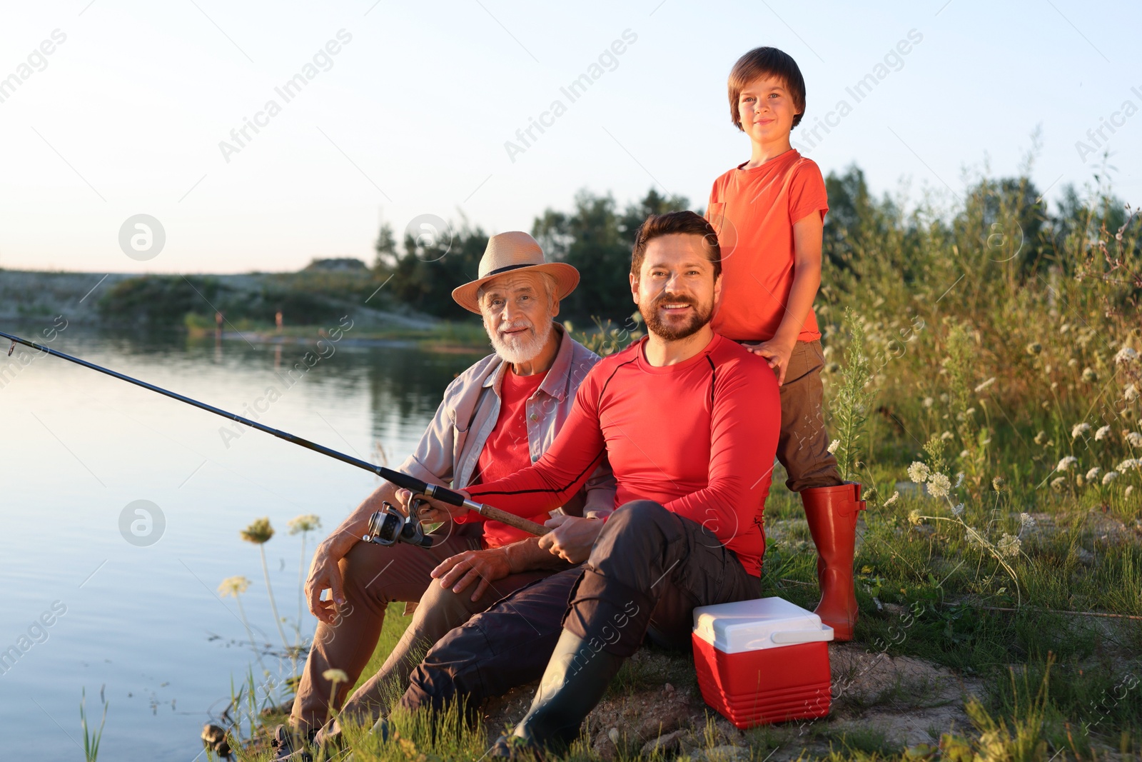 Photo of Smiling grandfather, father and his little son fishing together near river outdoors