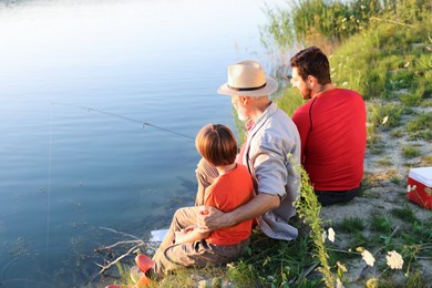 Photo of Grandfather, father and his little son fishing together near river outdoors