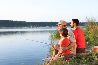 Photo of Smiling grandfather, father and his little son fishing together near river outdoors