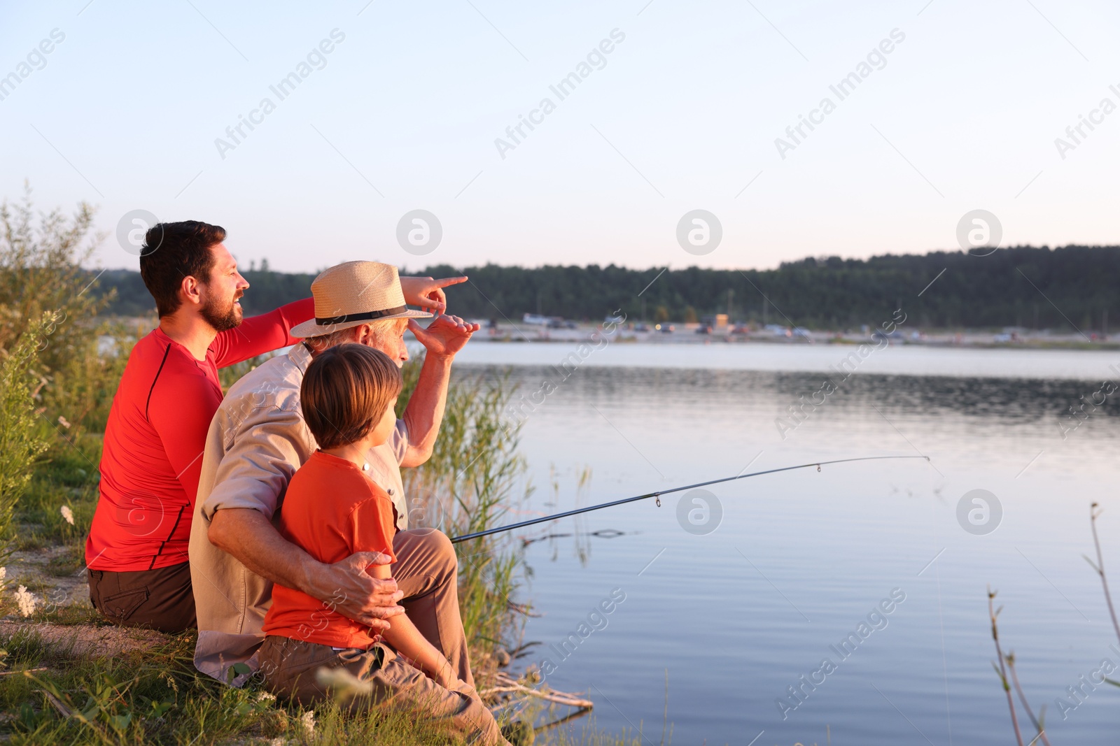 Photo of Smiling grandfather, father and his little son fishing together near river outdoors