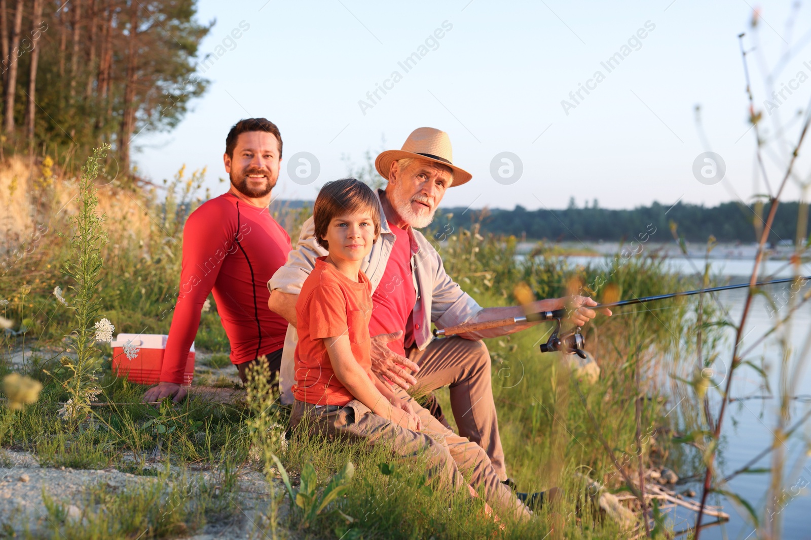 Photo of Grandfather, father and his little son fishing together near river outdoors
