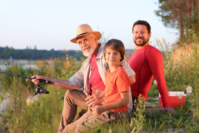 Photo of Smiling grandfather, father and his little son fishing together outdoors