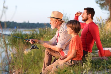 Photo of Grandfather, father and his little son fishing together outdoors