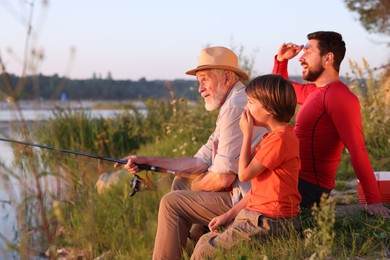 Photo of Grandfather, father and his little son fishing together outdoors