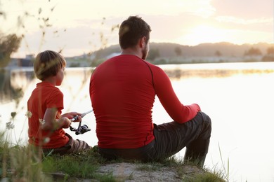 Photo of Father and his little son fishing together near river outdoors, back view
