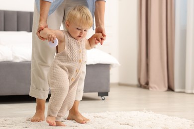 Photo of Mother teaching her baby how to walk at home, closeup. Space for text