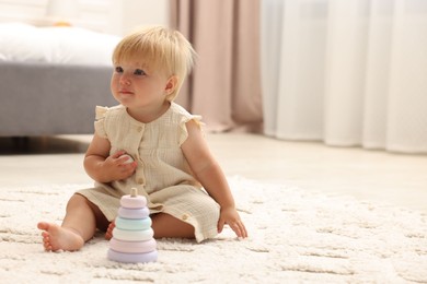 Photo of Cute baby girl in dress playing with toy on floor at home. Space for text