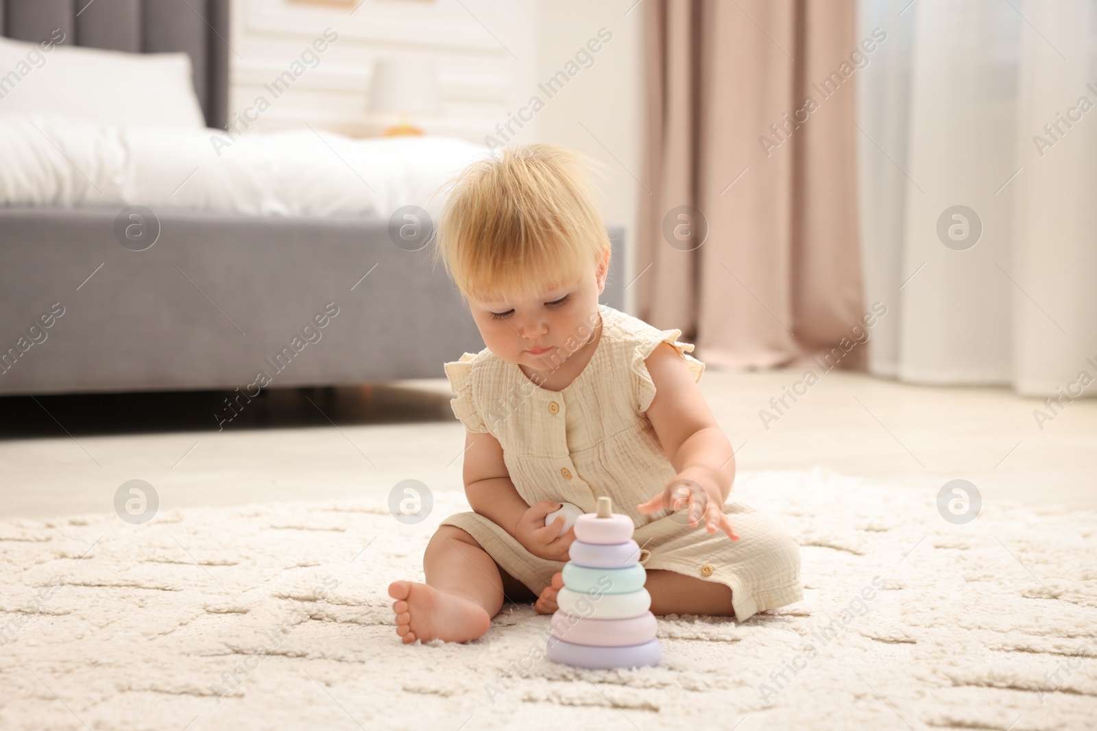 Photo of Cute baby girl in dress playing with toy on floor at home