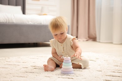 Photo of Cute baby girl in dress playing with toy on floor at home