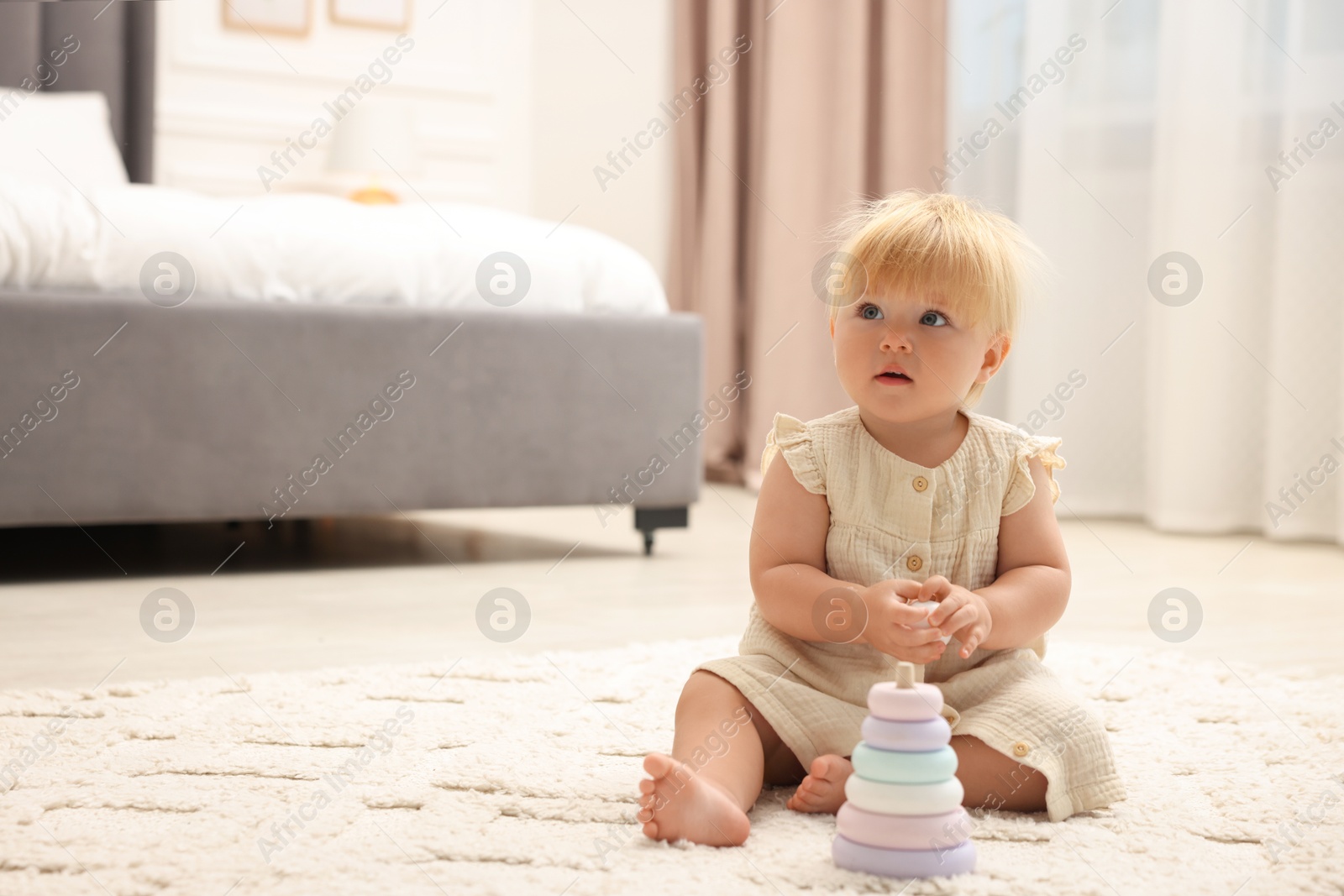 Photo of Cute baby girl in dress playing with toy on floor at home. Space for text
