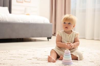 Photo of Cute baby girl in dress playing with toy on floor at home. Space for text