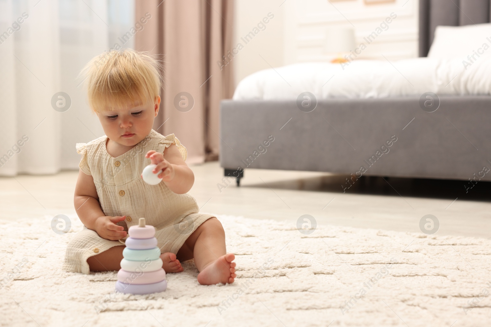 Photo of Cute baby girl in dress playing with toy on floor at home. Space for text