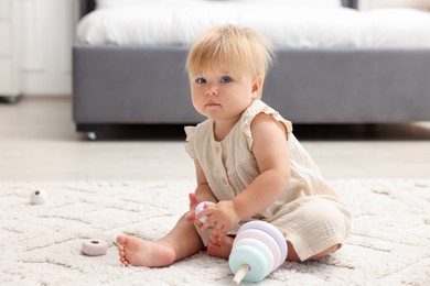 Photo of Cute baby girl in dress playing with toy on floor at home