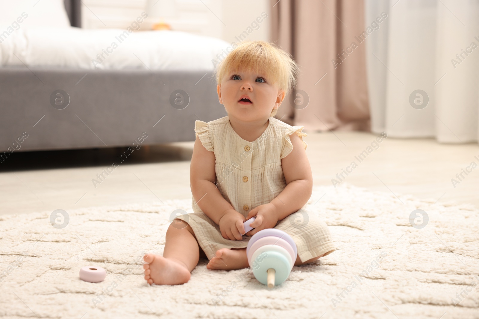 Photo of Cute baby girl in dress playing with toy on floor at home