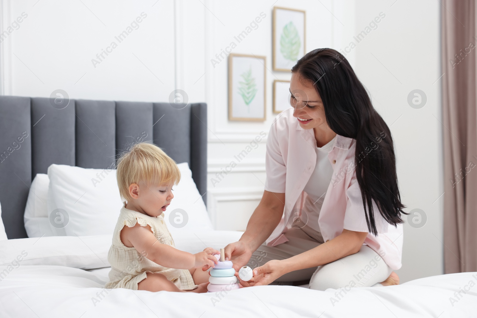Photo of Smiling mother playing with her cute baby girl on bed at home