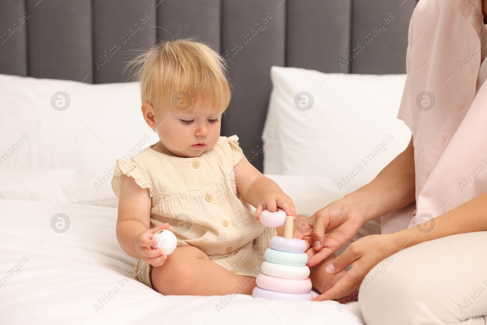 Cute baby girl and her mother playing with toy on bed at home, closeup Photo of Cute baby girl and her mother playing with toy on bed at home, closeup
