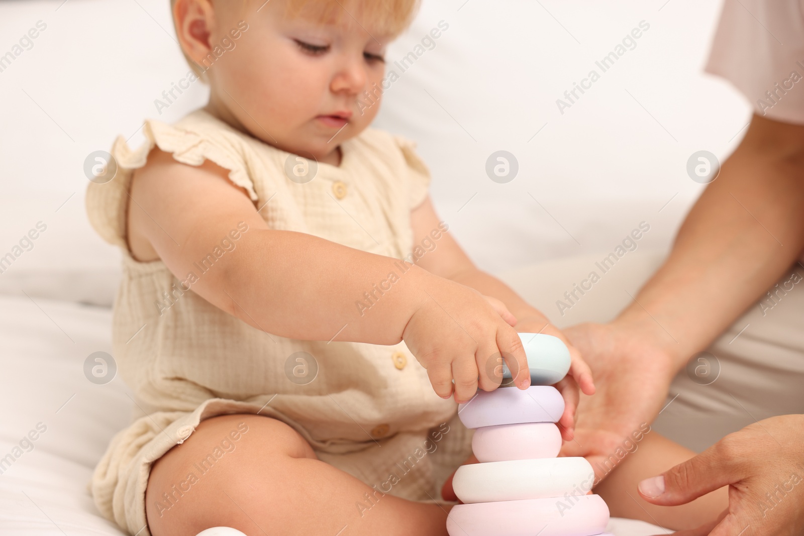 Cute baby girl and her mother playing with toy on bed at home, closeup Photo of Cute baby girl and her mother playing with toy on bed at home, closeup