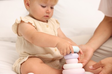 Photo of Cute baby girl and her mother playing with toy on bed at home, closeup