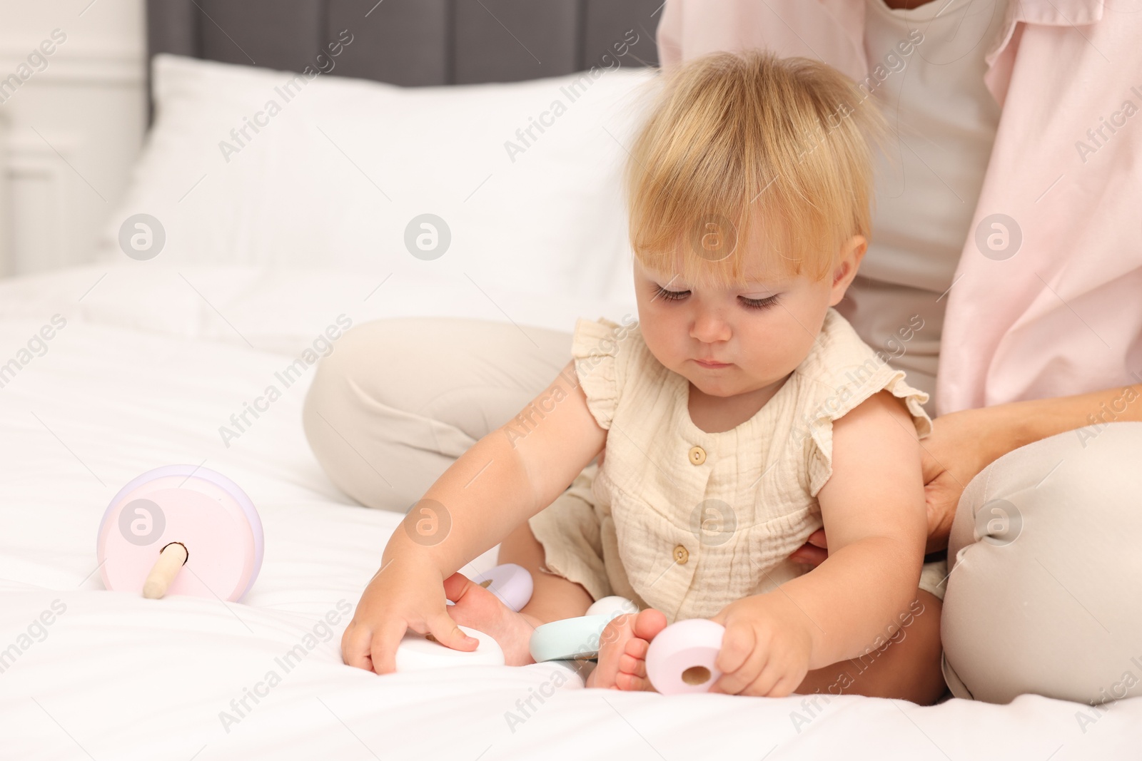 Cute baby girl and her mother playing with toy on bed at home, closeup Photo of Cute baby girl and her mother playing with toy on bed at home, closeup