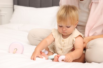 Photo of Cute baby girl and her mother playing with toy on bed at home, closeup