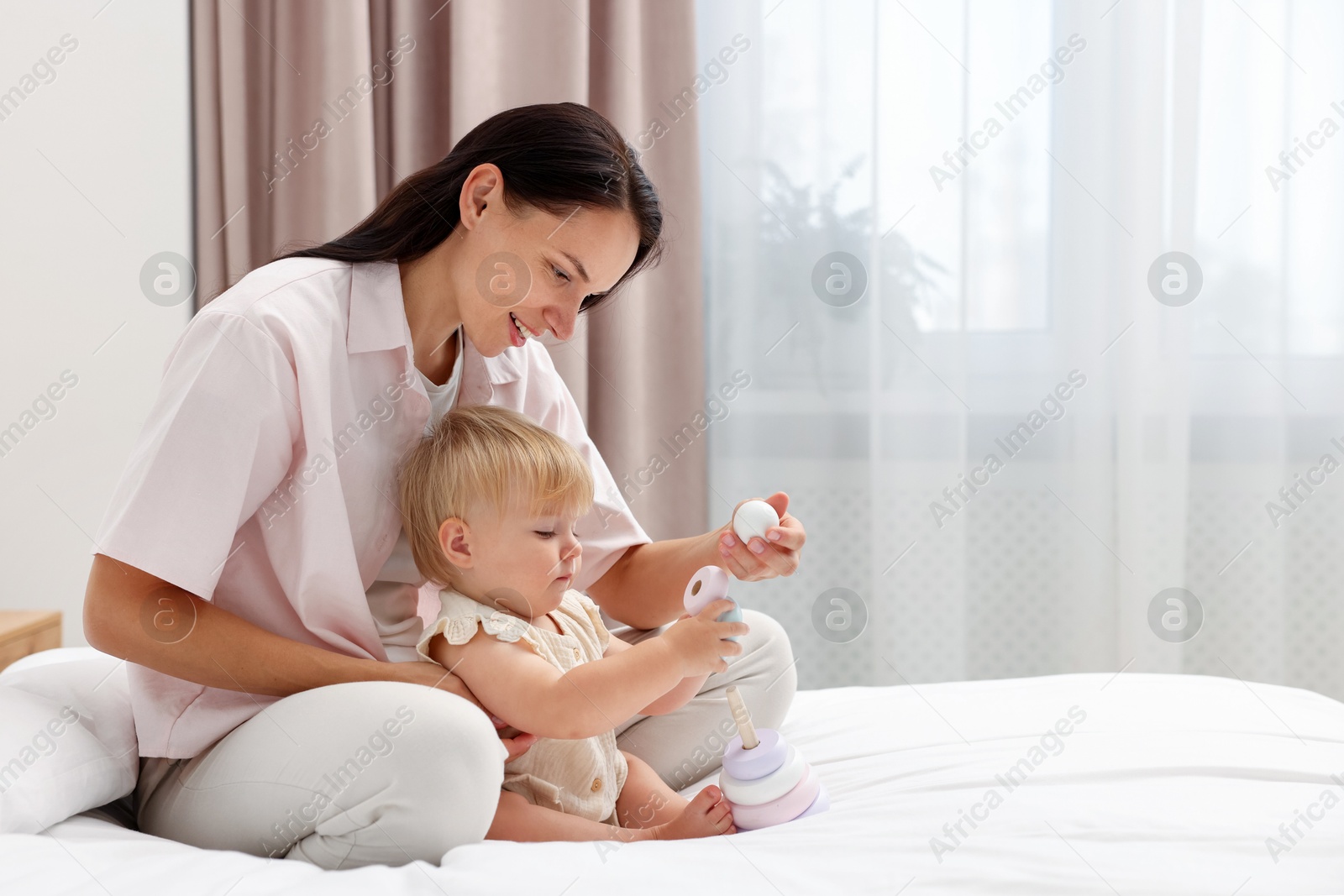 Smiling mother playing with her cute baby girl on bed at home. Space for text Photo of Smiling mother playing with her cute baby girl on bed at home. Space for text