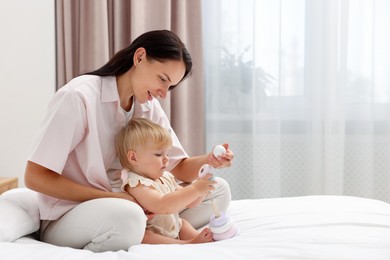 Photo of Smiling mother playing with her cute baby girl on bed at home. Space for text
